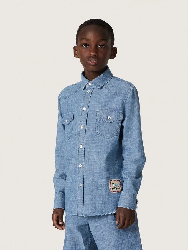 Journey unisex shirt in light blue cotton chambray with fringed hem and embroidered patch